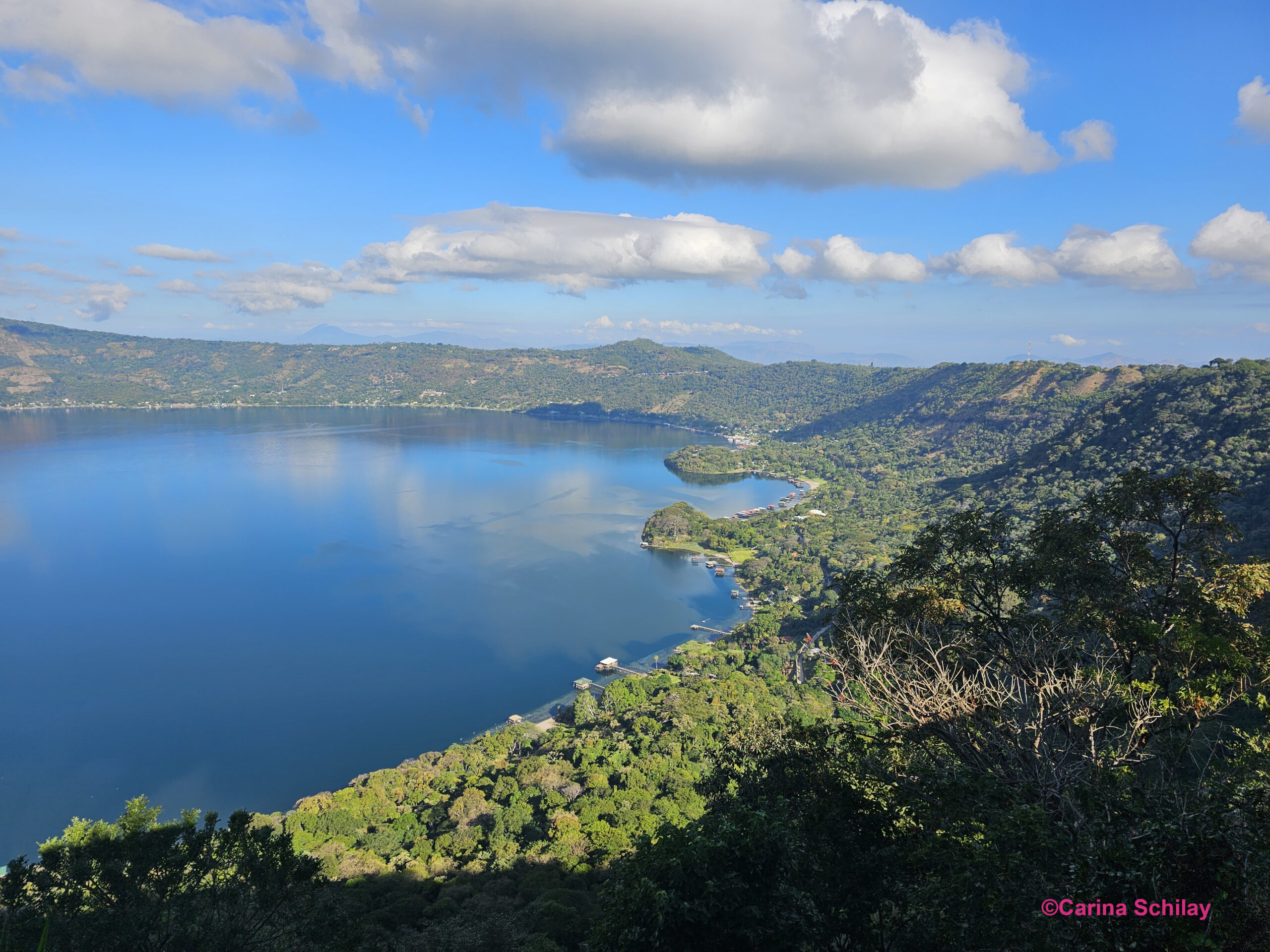 Die rechte Seite des Lago de Coatepeque, eingebettet in die üppigen grünen Hügel El Salvadors, spiegelt den friedvollen blauen Himmel wider.