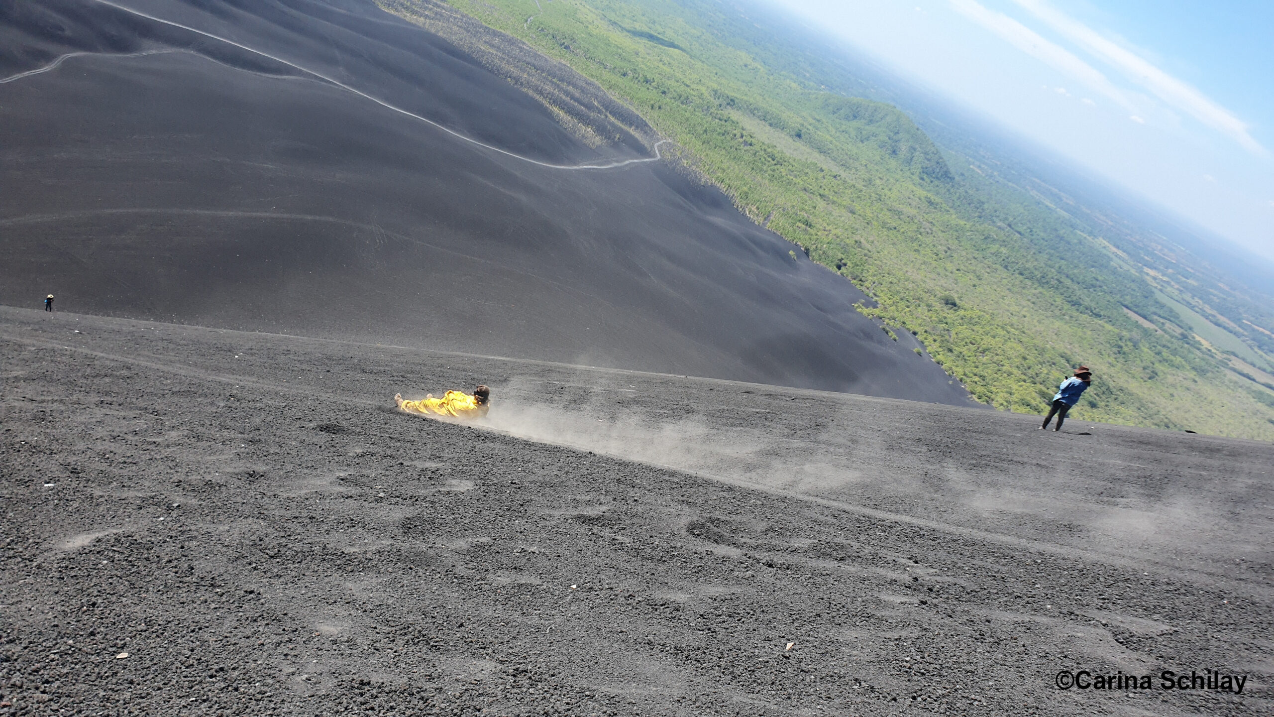 Abenteuerlustige Person rast auf einem gelben Sandboard den Cerro Negro hinunter, umgeben von der beeindruckenden Natur Nicaraguas.