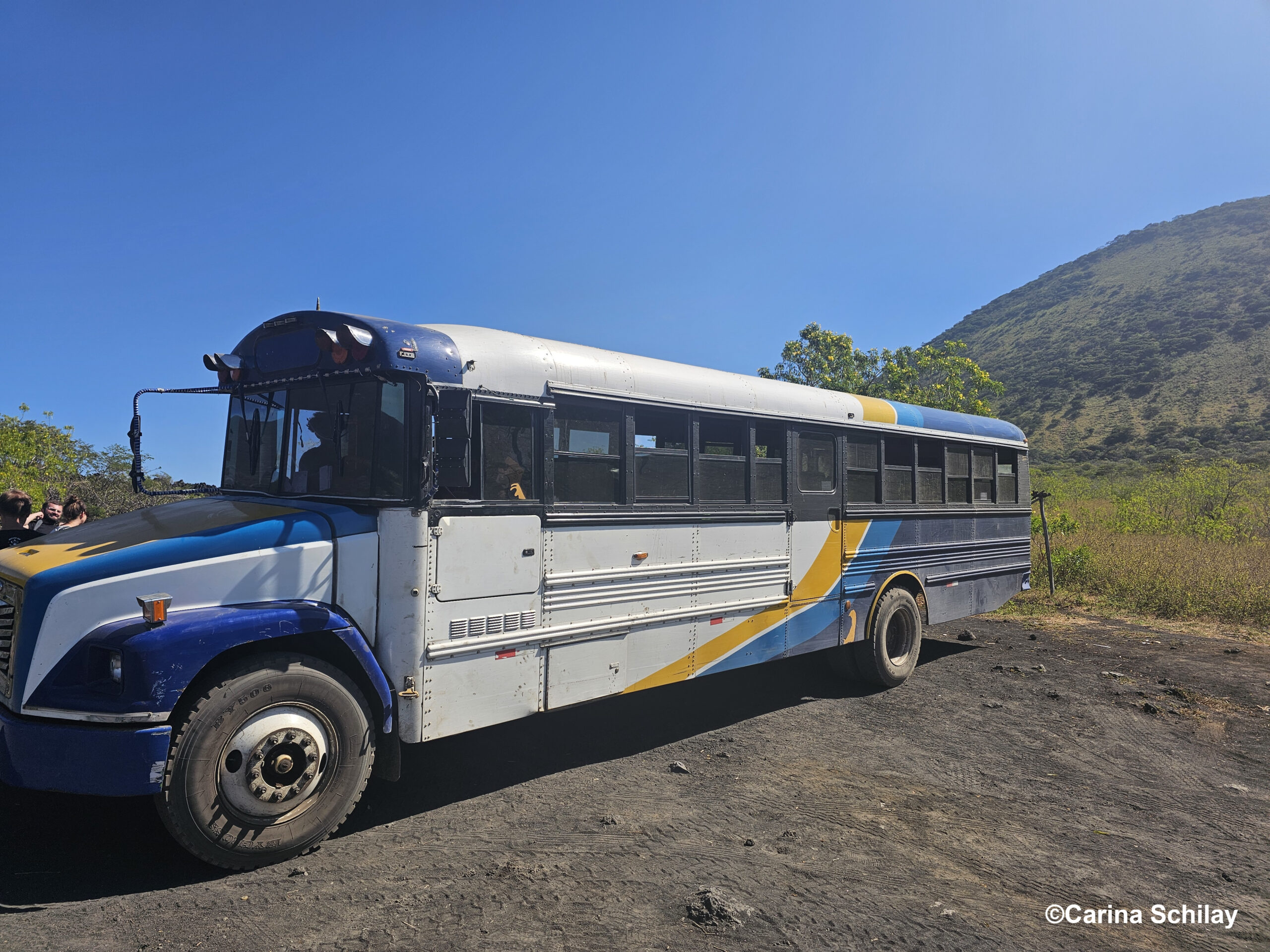 Ein alter Schulbus in Blau und Weiß parkt vor dem Cerro Negro in Nicaragua, bereit für das nächste Sandboarding-Abenteuer.