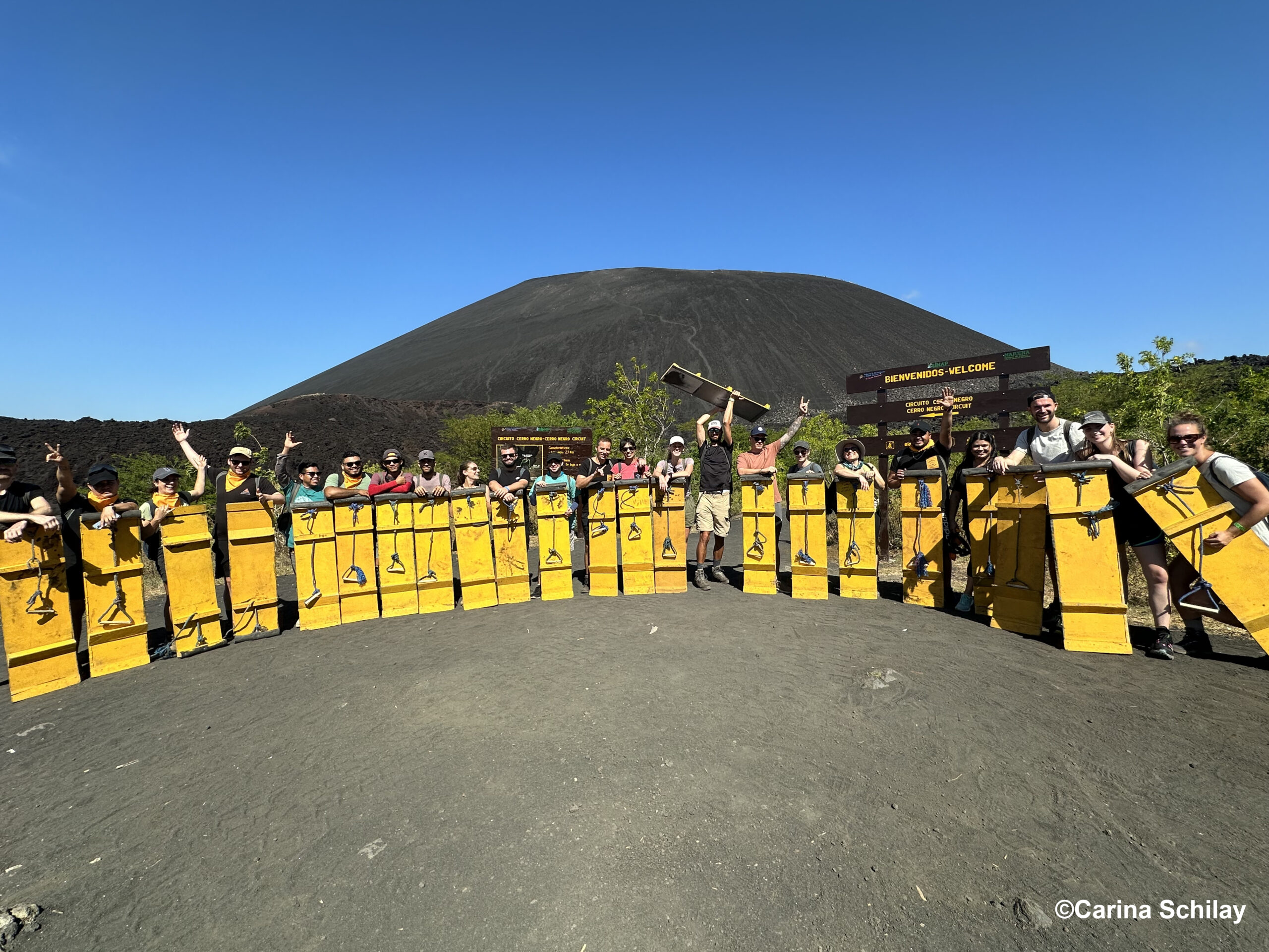 Gruppe abenteuerlustiger Menschen bereitet sich mit gelben Sandboards am Fuß des beeindruckenden Cerro Negro in Nicaragua auf das Sandboarding vor.