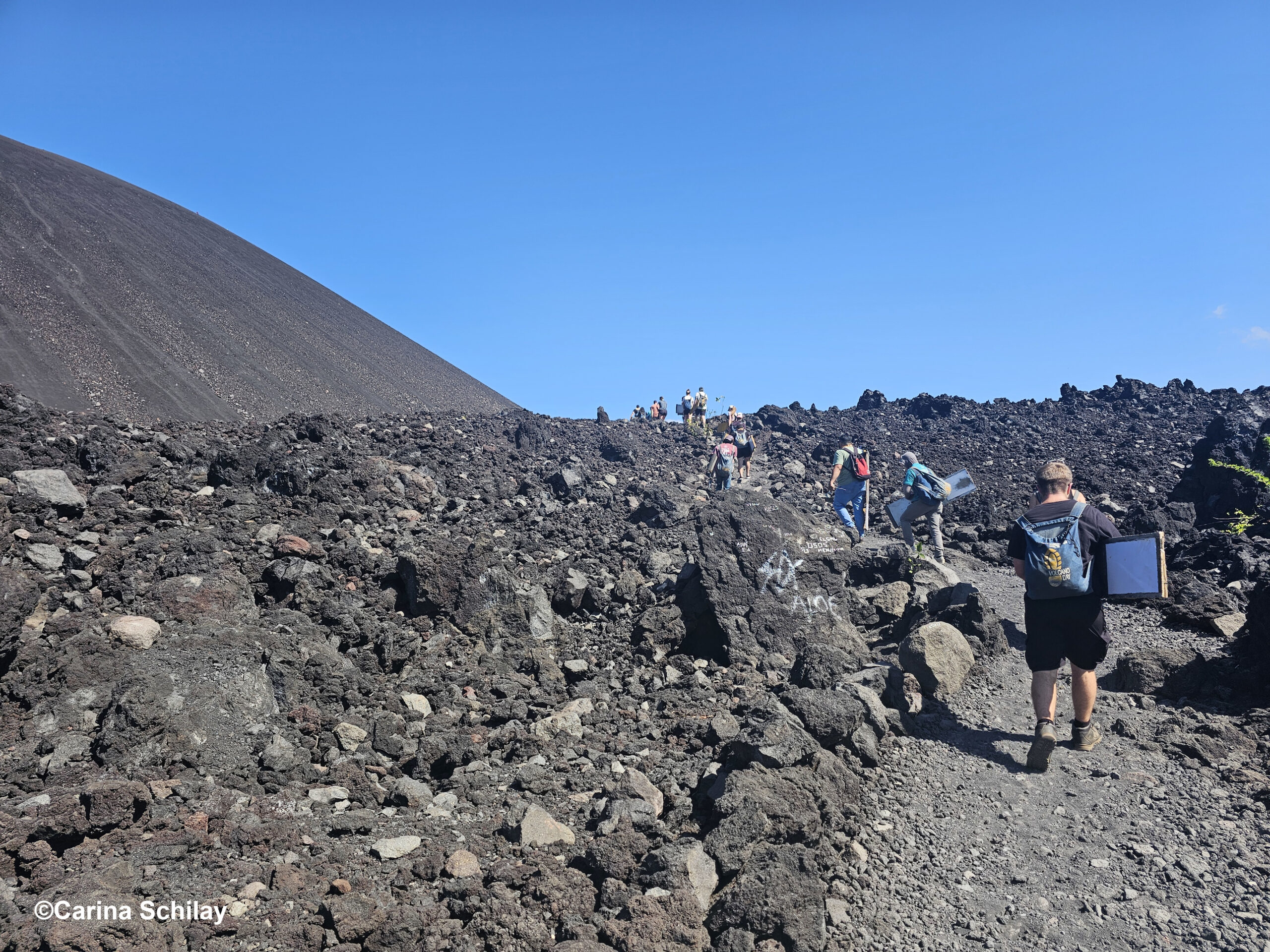 Mehrere Wanderer tragen ihre Sandboards den Cerro Negro hinauf, bereit für das Sandboarding-Abenteuer.