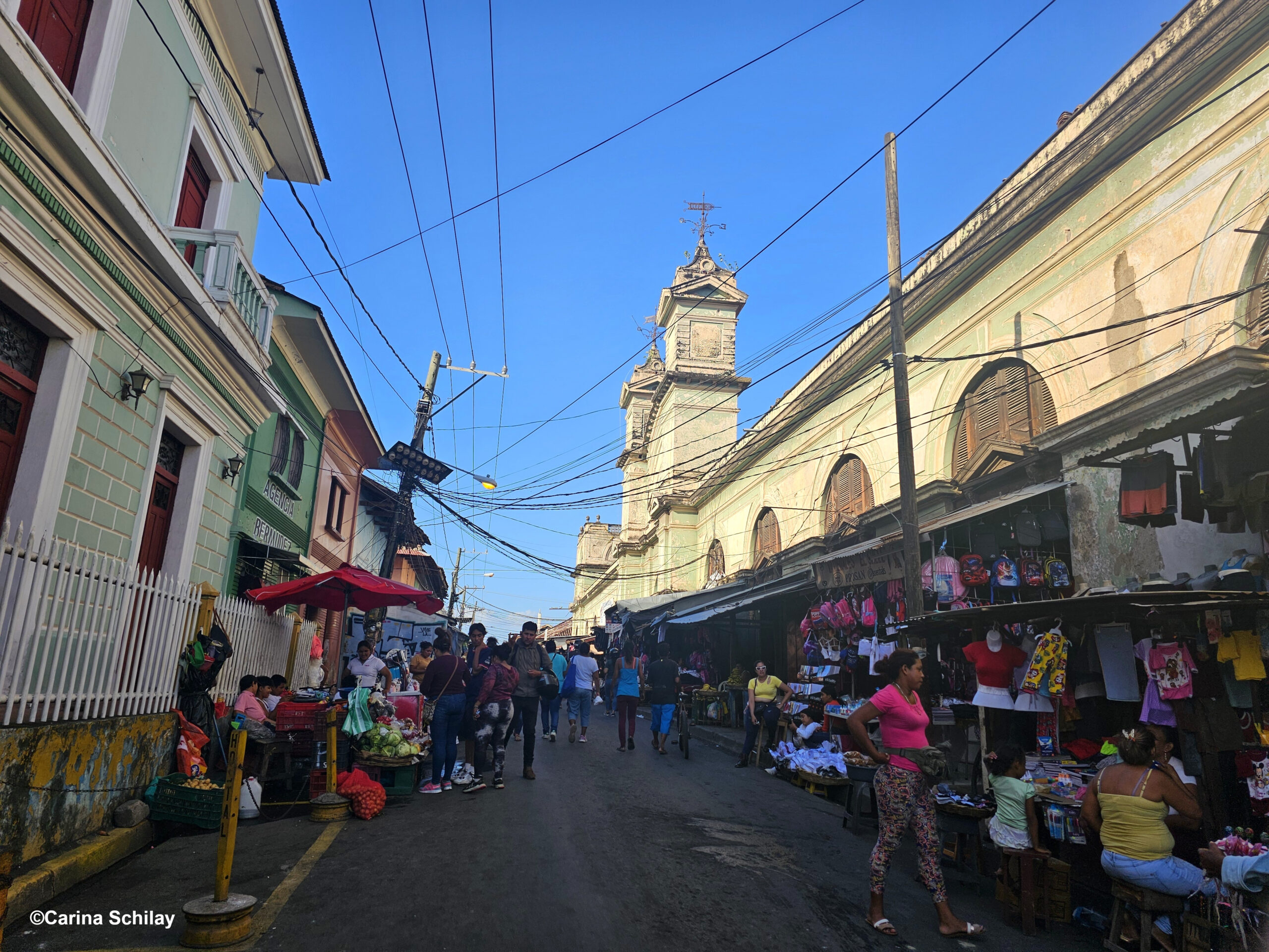 Lebendiger Markttreiben auf einer Straße in Granada mit historischer Kirche im Hintergrund.