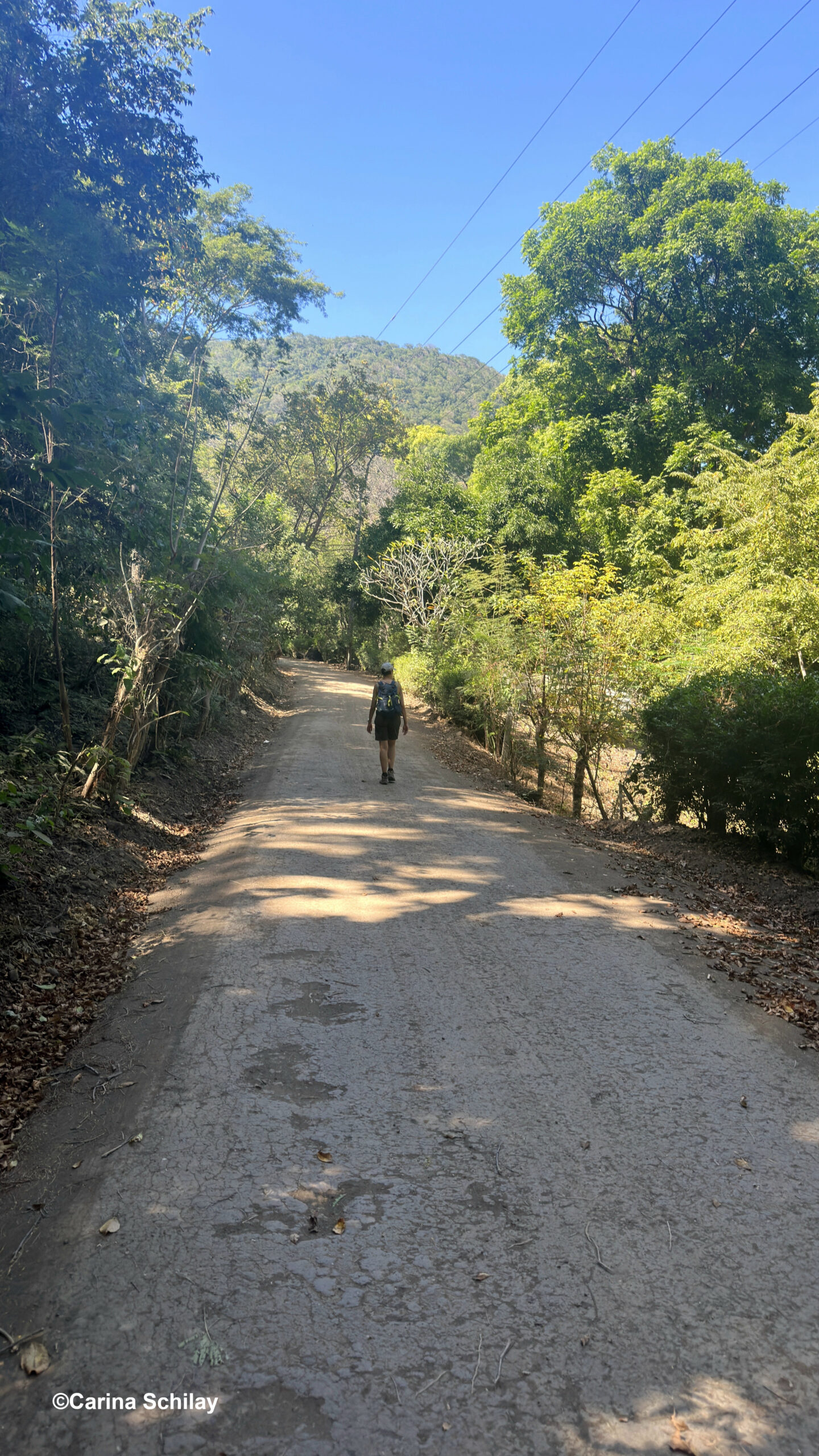 Wanderer auf einsamer Schotterstraße umgeben von grüner Natur unter strahlend blauem Himmel in Masaya, Nicaragua.