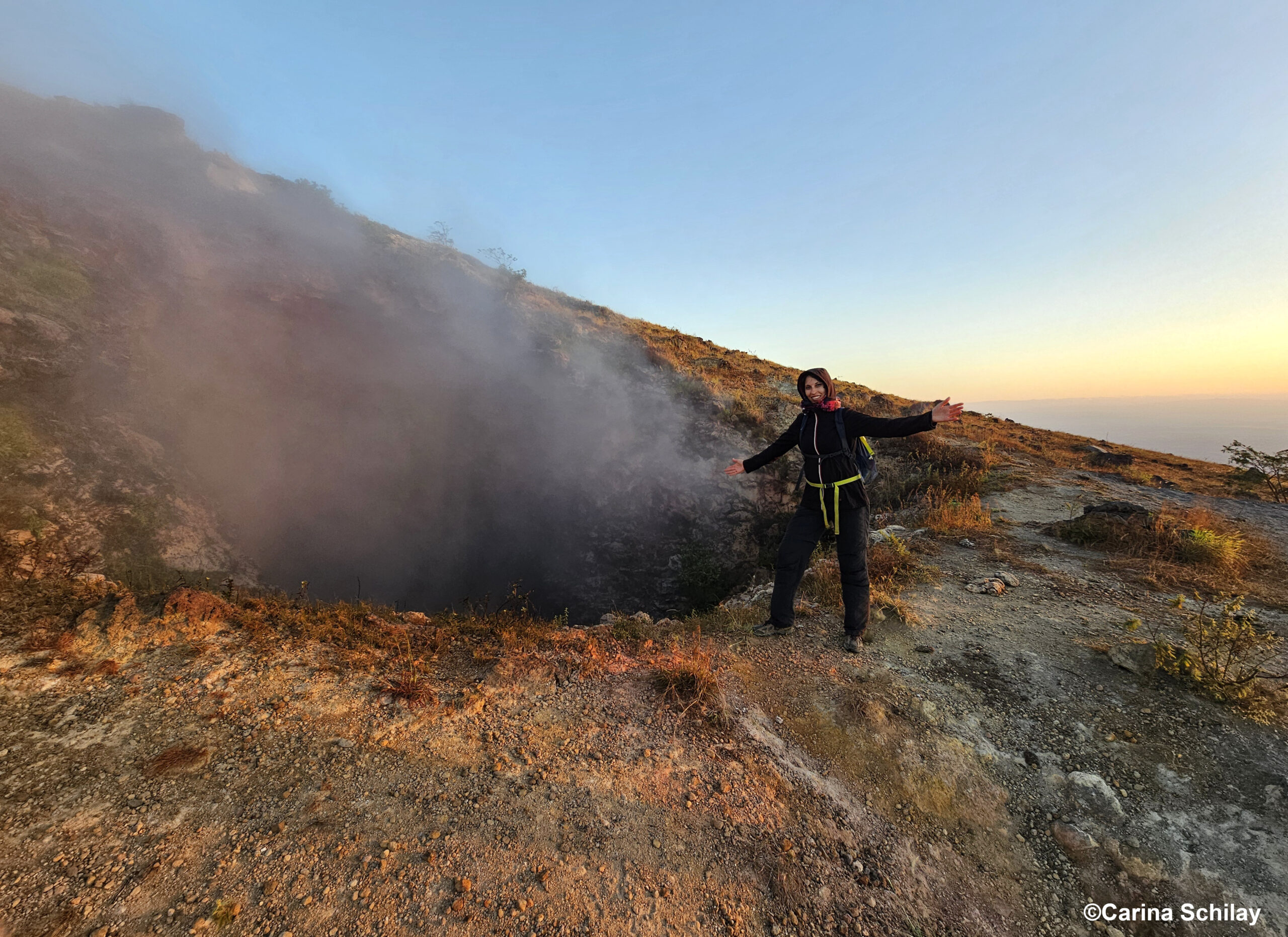 Person steht vor dem kleinen Krater des El Hoyo, aus dem warmer Rauch aufsteigt.