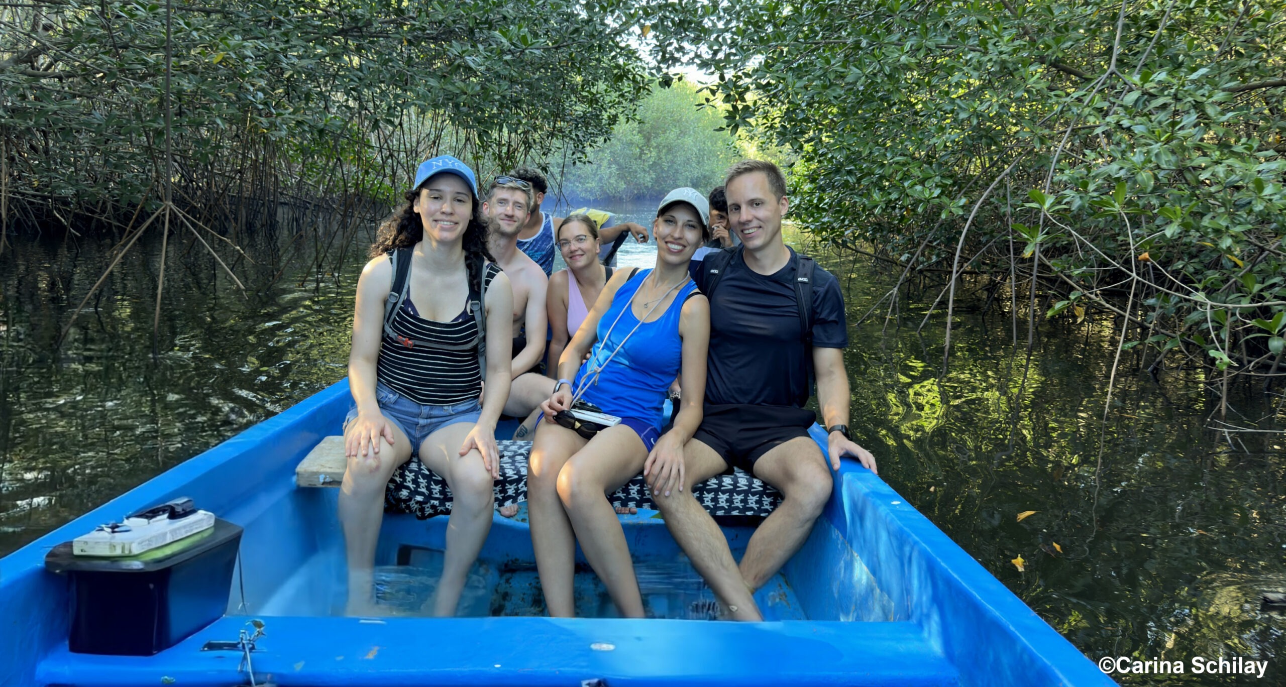 Gruppe von sechs Personen in einem blauen Boot, das durch Mangroven gleitet