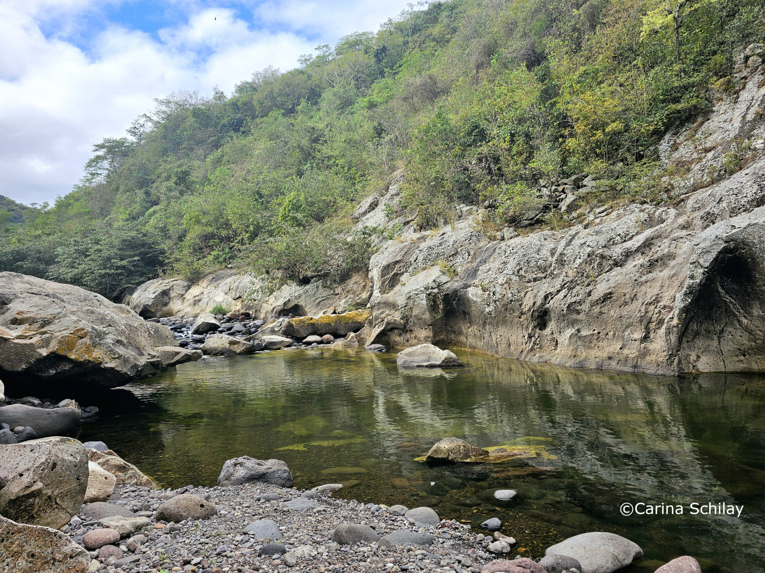 Ein ruhiger Flussabschnitt des Rio Coco, gesäumt von felsigen Klippen und grüner Vegetation unter einem teilweise bewölkten Himmel.