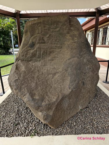 Ein großer Stein mit alten Schnitzereien, der unter einem Schutzdach ausgestellt ist.